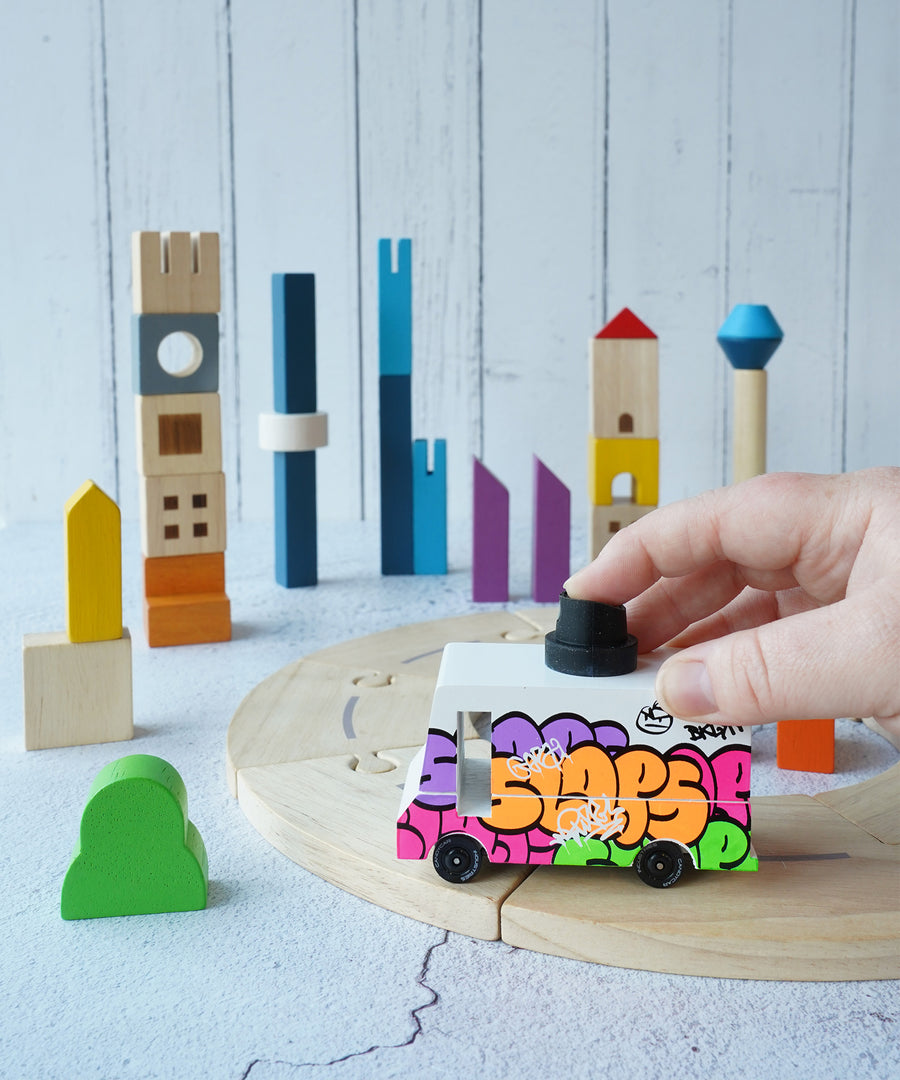 The PlanToys Wooden Cityscape Blocks set up in a play scene with the PlanToys wooden road and a Candylab graffiti van. 