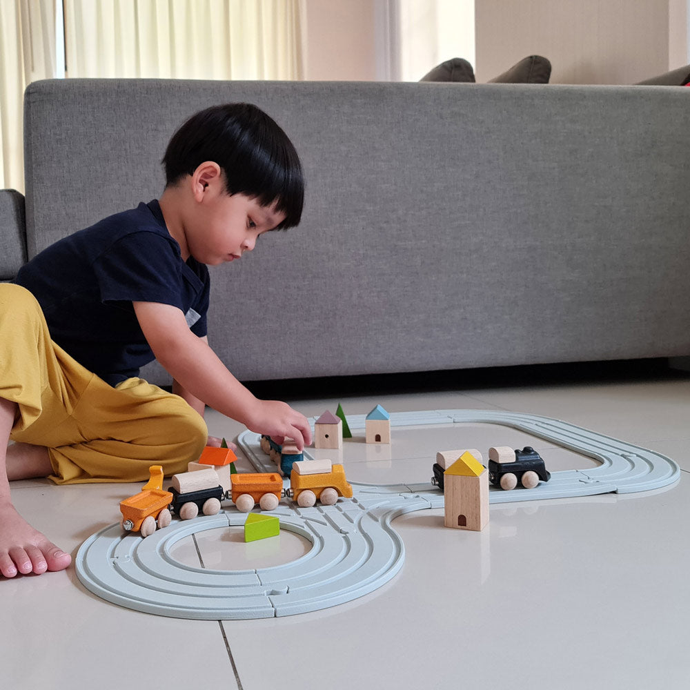 Boy sat on a grey floor playing with the Play Toys plastic free wooden train toys on the plan world road and train track set