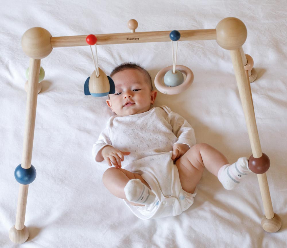 A baby laying underneath the PlanToys Play Gym Orchard. 