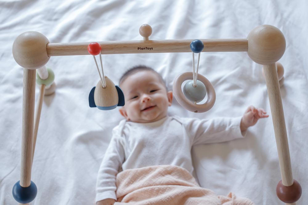 A baby laying underneath the PlanToys Play Gym Orchard .