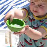 A child playing with the green bowl from the PlanToys Fountain Bowl Set, water can be seen pouring from the holes in side of the bowl.  