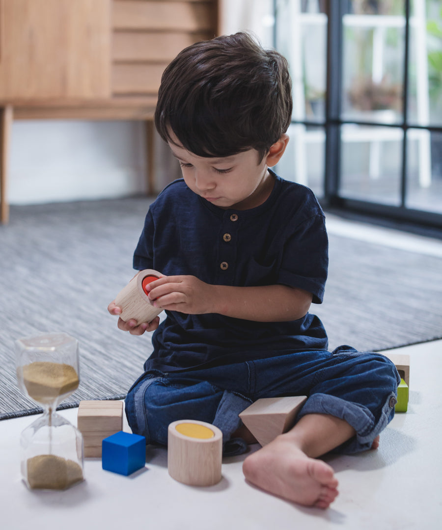 A child sitting on a floor playing with the PlanToys Geo Matching Blocks. 