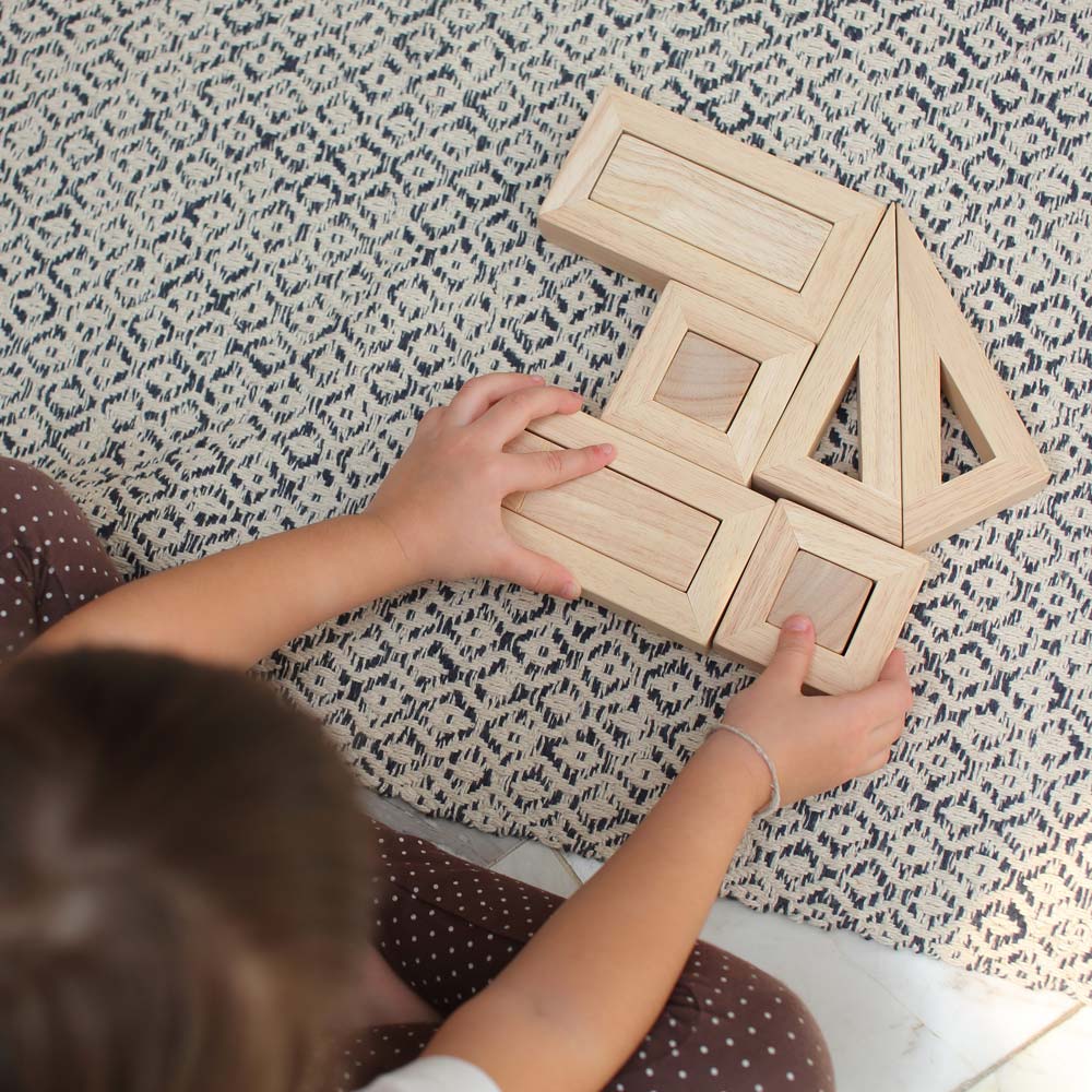 An overhead view of a child sitting on a patterned rug playing with the PlanToys Hollow Blocks.