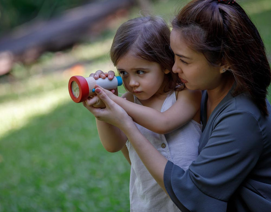 A child and and adult using the PlanToys Kaleidoscope. The adult id helping the child hold it up to their eye. 