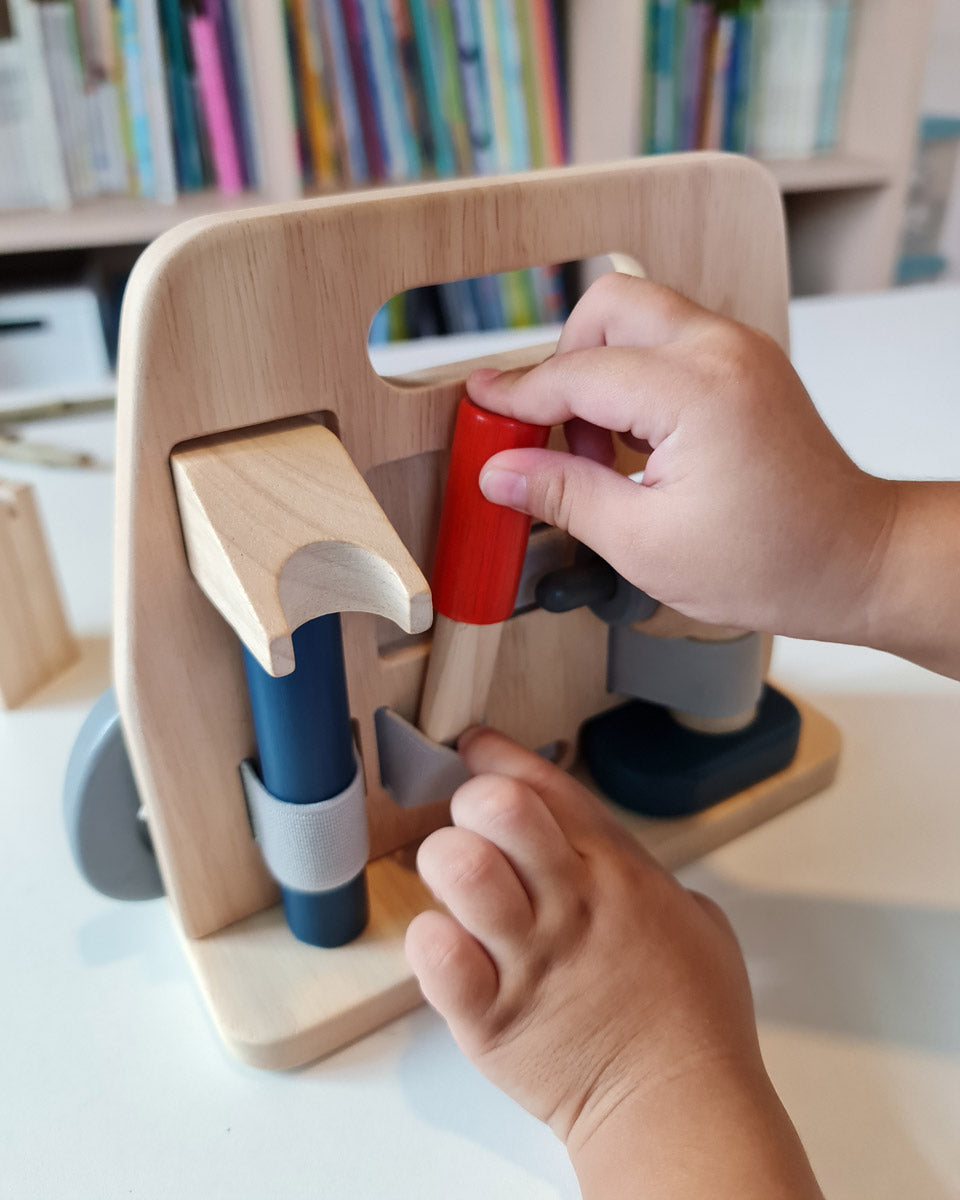 Close up of a hand pulling out a tool from the Plan Toys plastic free wooden carpenter role play toy set