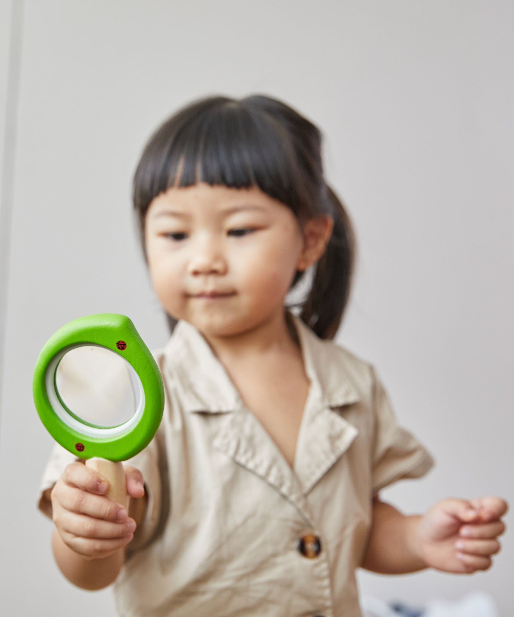 A child holding a PlanToys Leaf Magnifier toy in their hand.