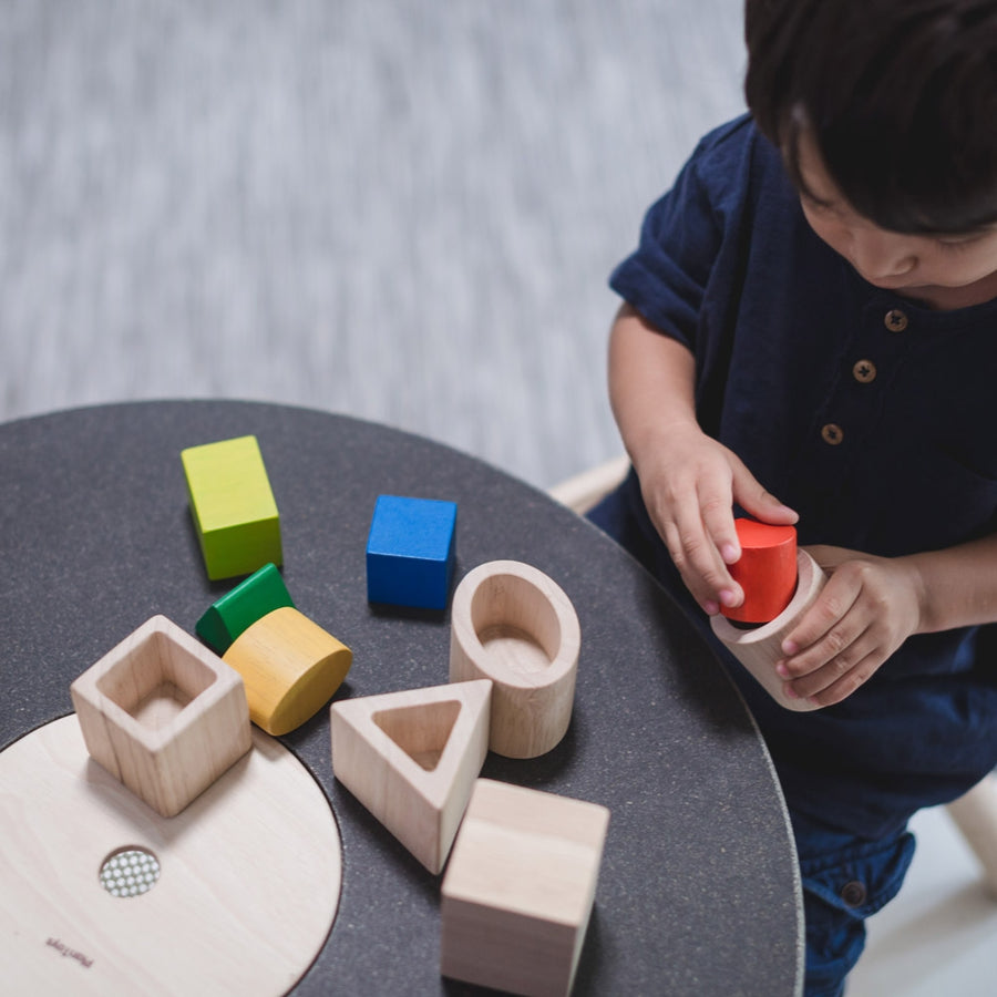 A child sitting at a table playing with the PlanToys Geo Matching Blocks. 