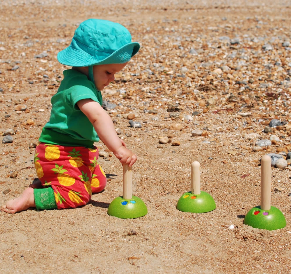 A child on the beach playing with the PlanToys Meadow Ring Toss. 
