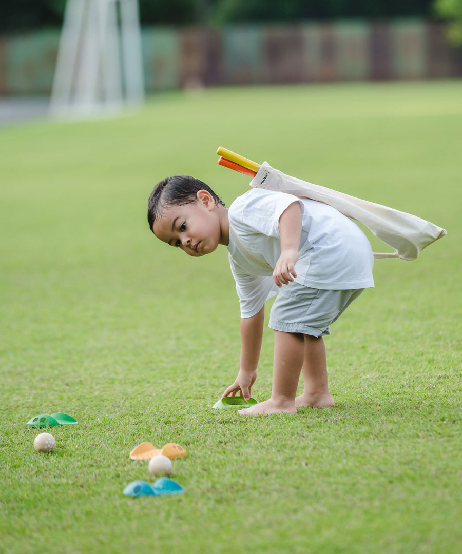 A child playing with a the PlanToys Mini Golf Set outside on grass. He is picking up one of the green wooden hole. 