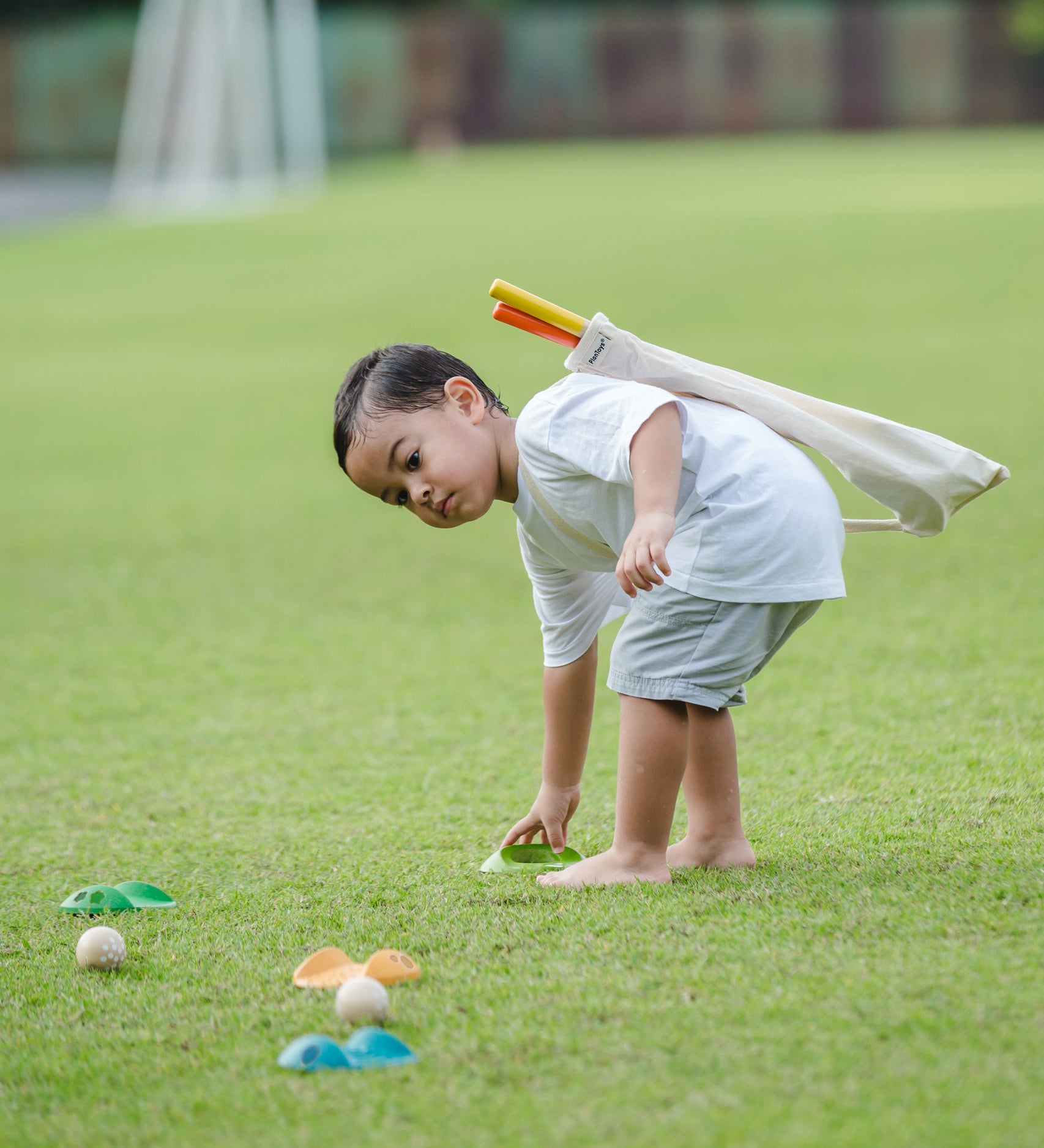 A child playing with a the PlanToys Mini Golf Set outside on grass. He is picking up one of the green wooden hole. 