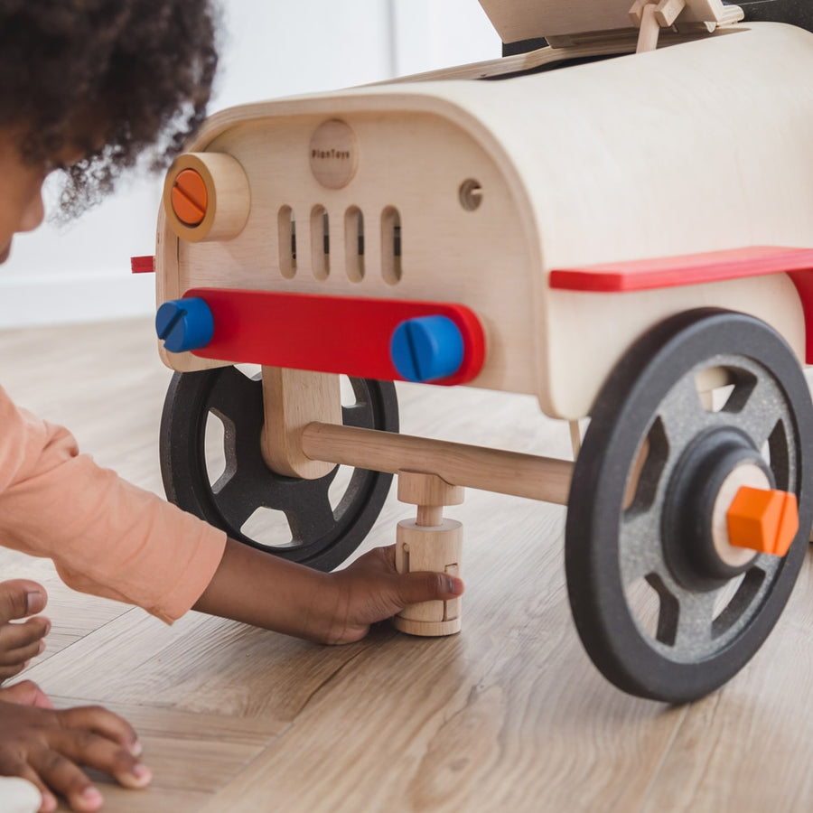 A close up of a child playing with the PlanToys Motor Mechanic role play toy. They can be seen putting the wooden jack toy underneath the front of the car. 