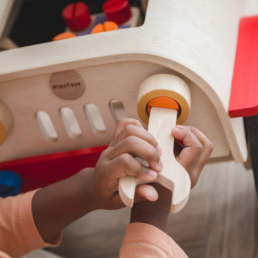 A close up of a child playing with the headlights on the PlanToys Motor Mechanic role play toy.