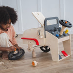 A child playing with the PlanToys Motor Mechanic role play toy. They have taken one of the wheels off the car. 