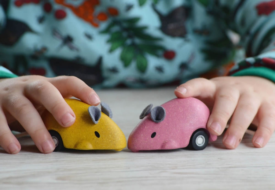 PlanToys Wooden Pull-Back Mouse Toys in yellow and pink in a child's hands.