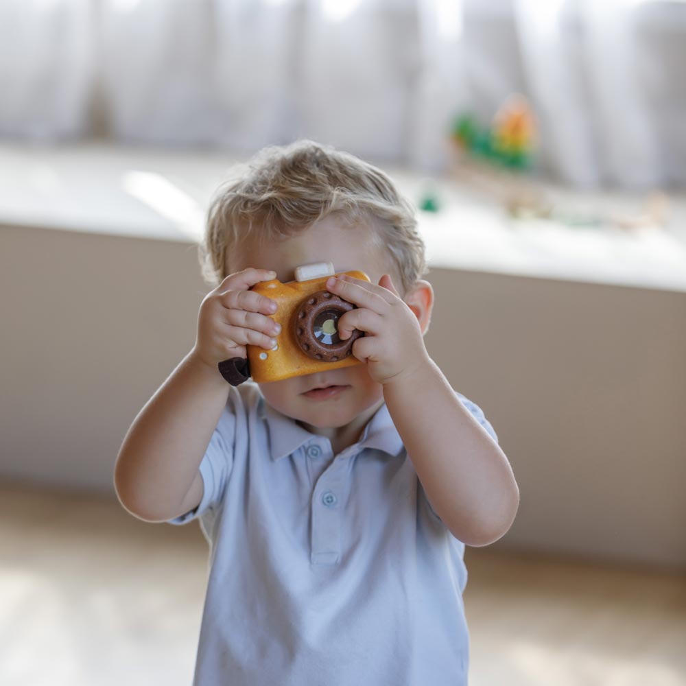 A child playing with the PlanToys Yellow My First Camera holding up the toy cameras to their eyes.