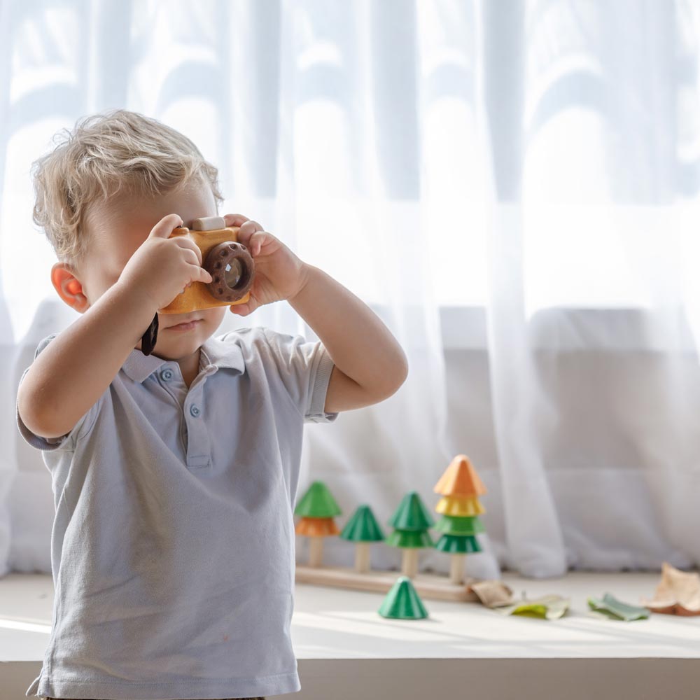 A child playing with the PlanToys Yellow My First Camera holding up the toy cameras to their eyes.