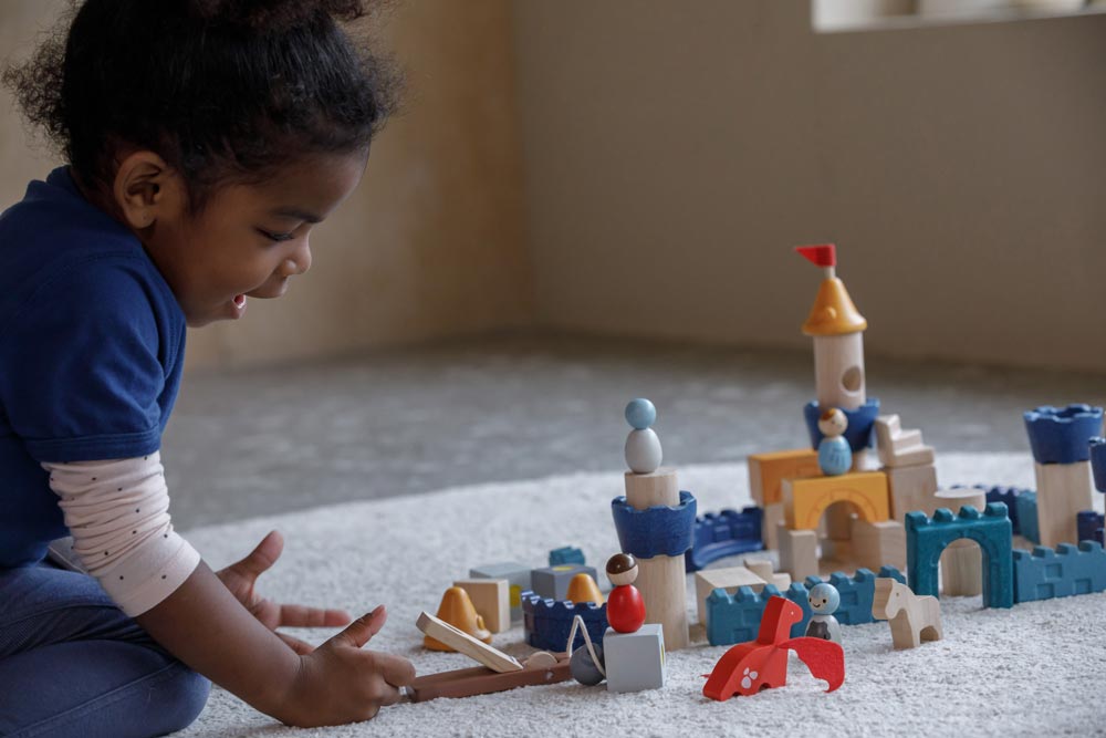 A child playing sitting on a rug playing with the PlanToys Castle Building Blocks set. 