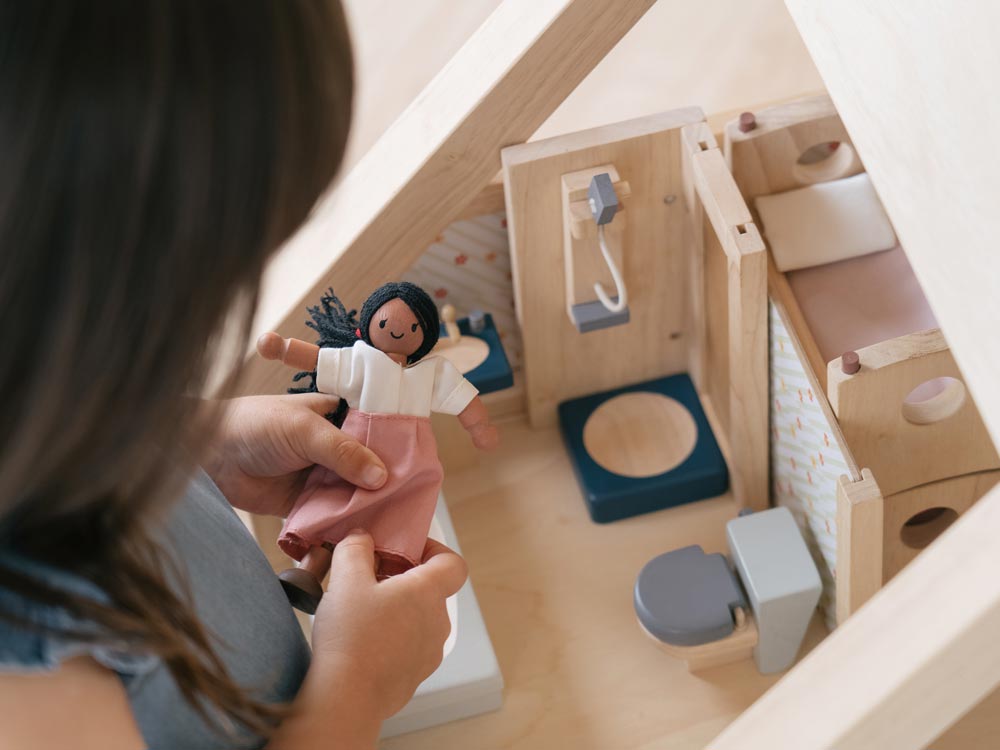 A child holding a wooden dolly, the PlanToys Bathroom Dolls House Furniture can be seen in the background.