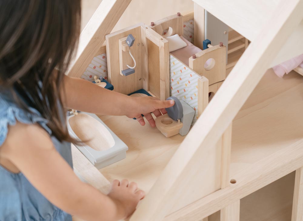 A child playing with the PlanToys Bathroom Dolls House Furniture that has been set up in a wooden dolls house.