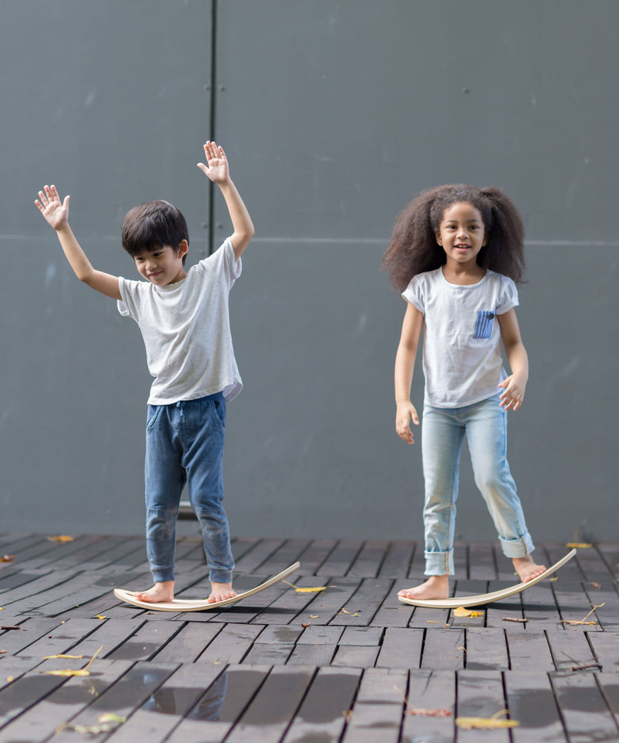 Two children, each standing upon a PlanToys Balance Board.