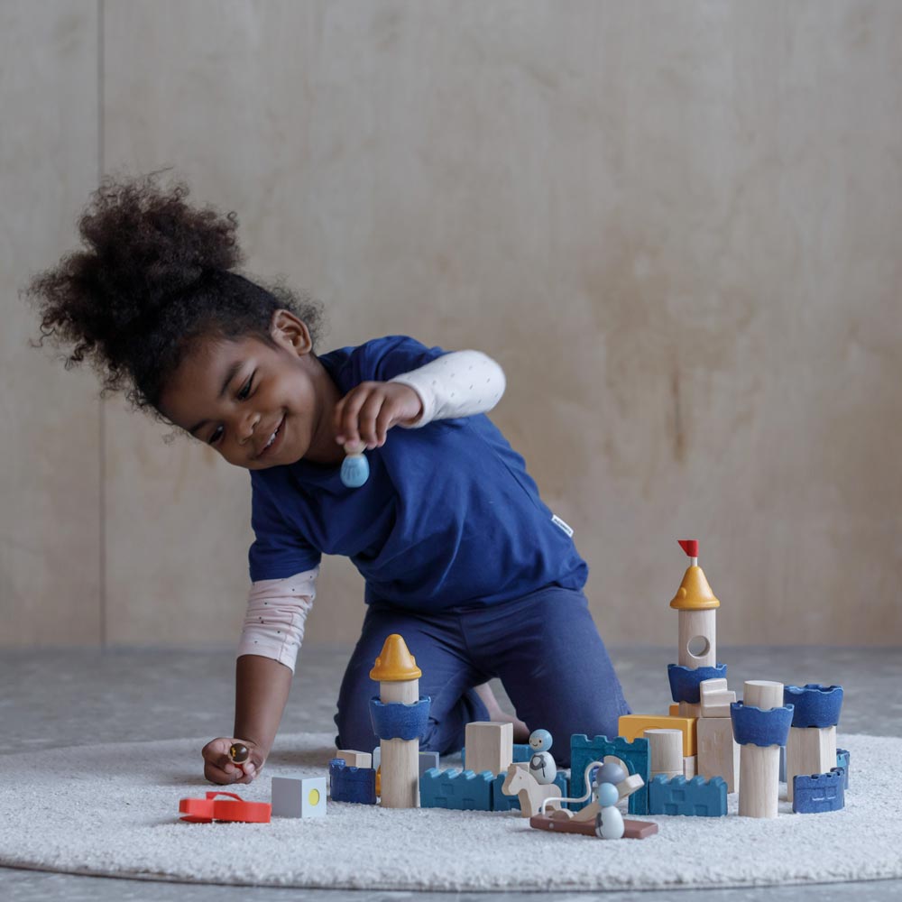 A child playing sitting on a rug playing with the PlanToys Castle Building Blocks set. 