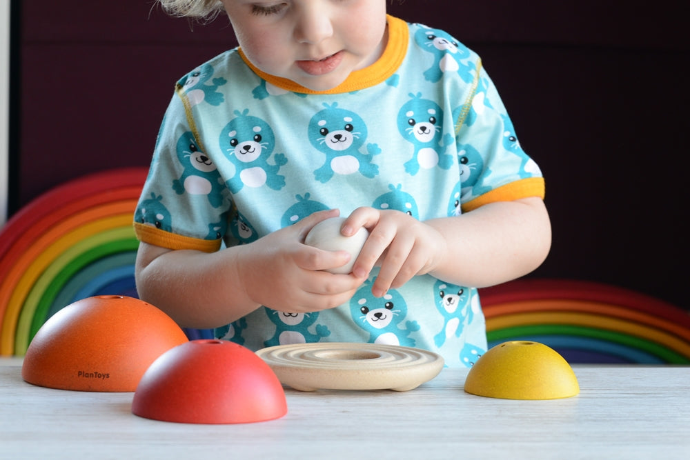 A child playing with the PlanToys Chicken Nesting Toy. The pieces have all been taken off the wooden bas and the child is holding on to the egg.