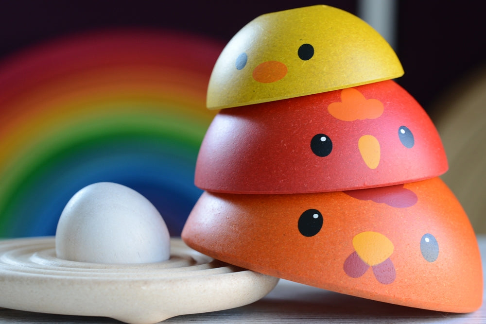 A close up of the A child playing with the PlanToys Chicken Nesting Toy. The egg has been placed on the wooden base with the three wooden chickens stacked up besides the base. 