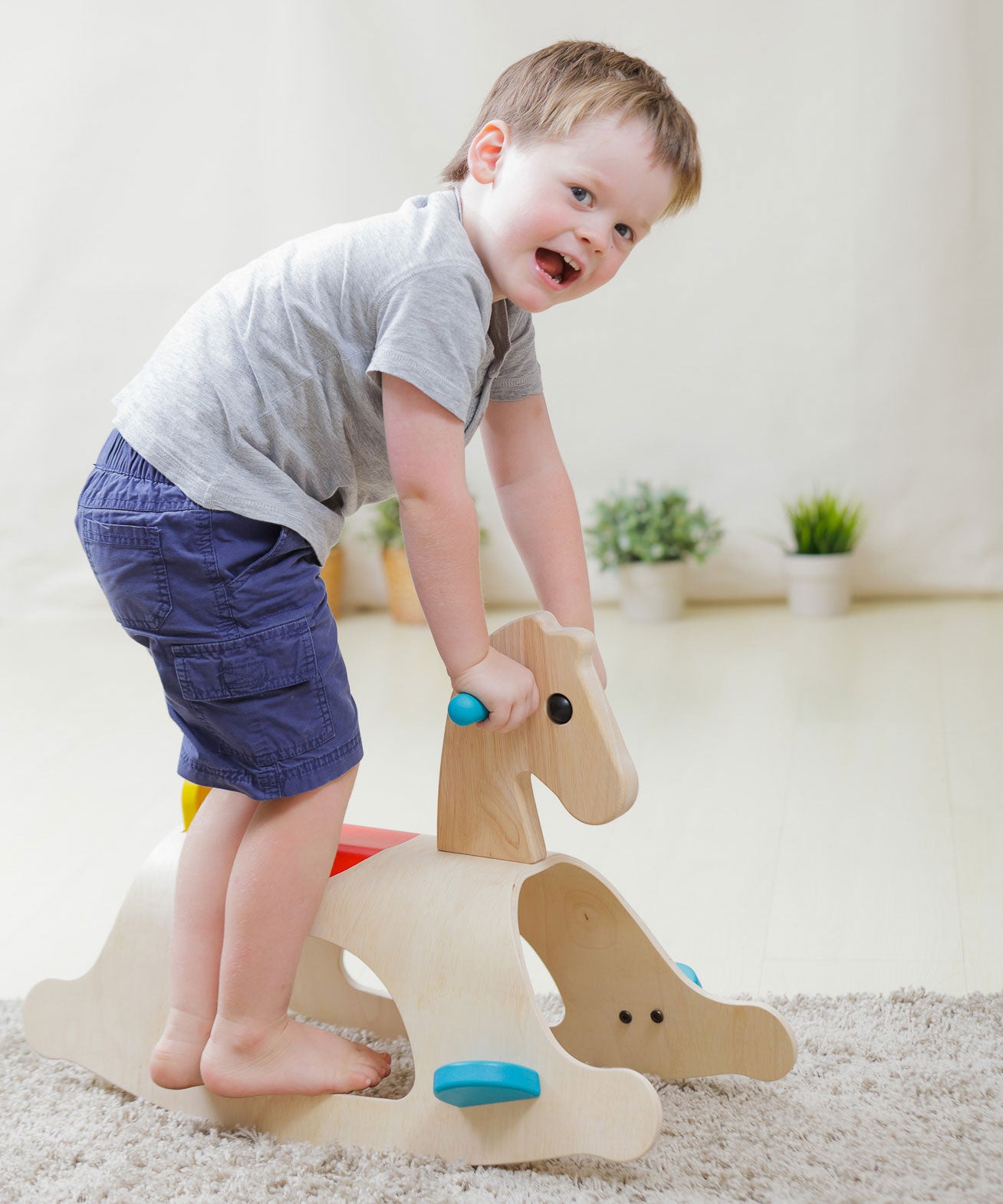 A child standing on the side of the PlanToys Palomino Rocking Horse. 