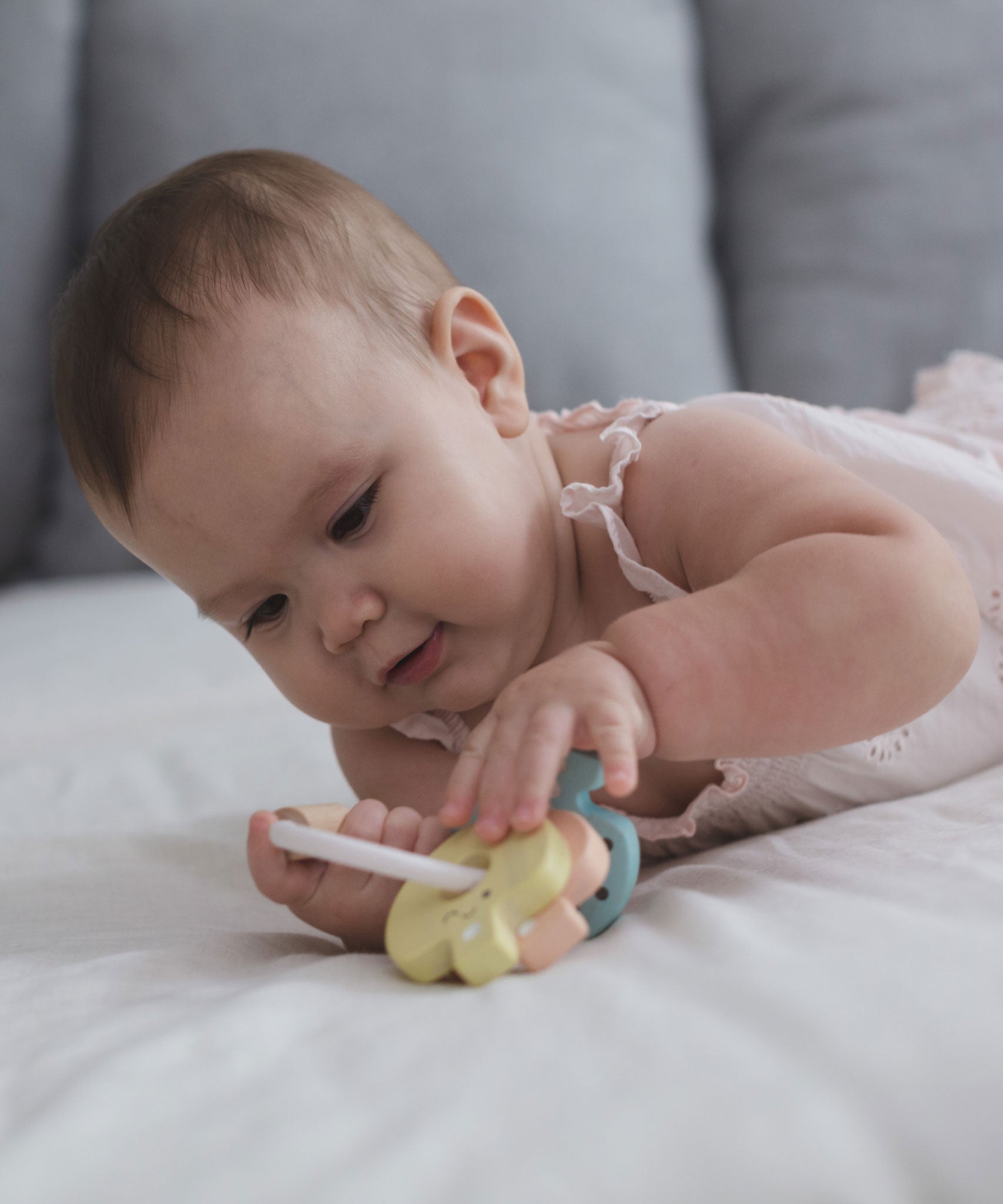 A baby laying on their tummy playing with the PlanToys Pastel Baby Key Rattle. 