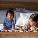 Two children playing with PlanToys vehicles whilst laying on their fronts on a bed. 