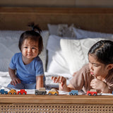 Two children playing with PlanToys vehicles whilst laying on their fronts on a bed. 