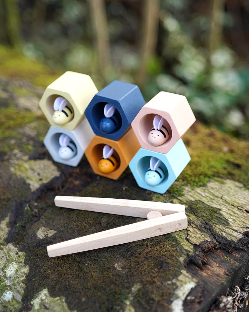 The PlanToys Bee Hives in the Orchard colour way placed on a moss covered log outdoors. 