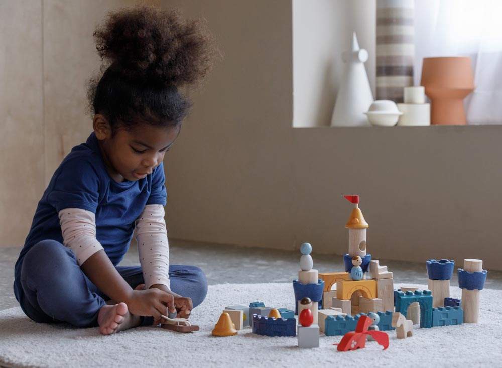 A child playing sitting on a rug playing with the PlanToys Castle Building Blocks set. 