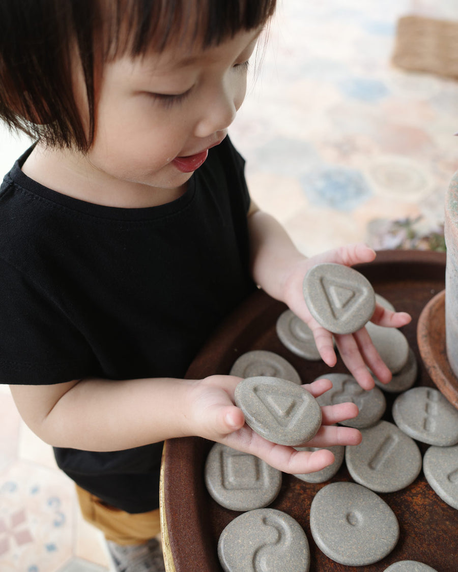 Girl tracing around the carvings in the Plan Toys wooden tactile stones on a dark brown table