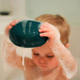 A playing with Plan Toys Polar Bear Sailing Boat in the bath. The boat is covered in soapy suds. 