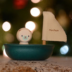 The Plan Toys Polar Bear Sailing Boat pictured with fairy lights behind. The blurred background is showing the bokeh from the lights. 