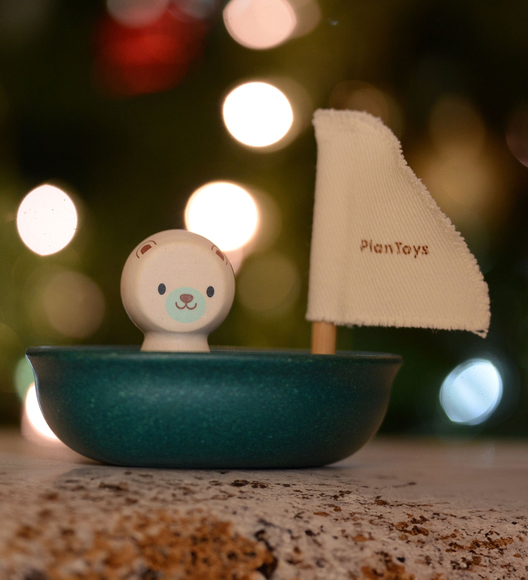 The Plan Toys Polar Bear Sailing Boat pictured with fairy lights behind. The blurred background is showing the bokeh from the lights. 