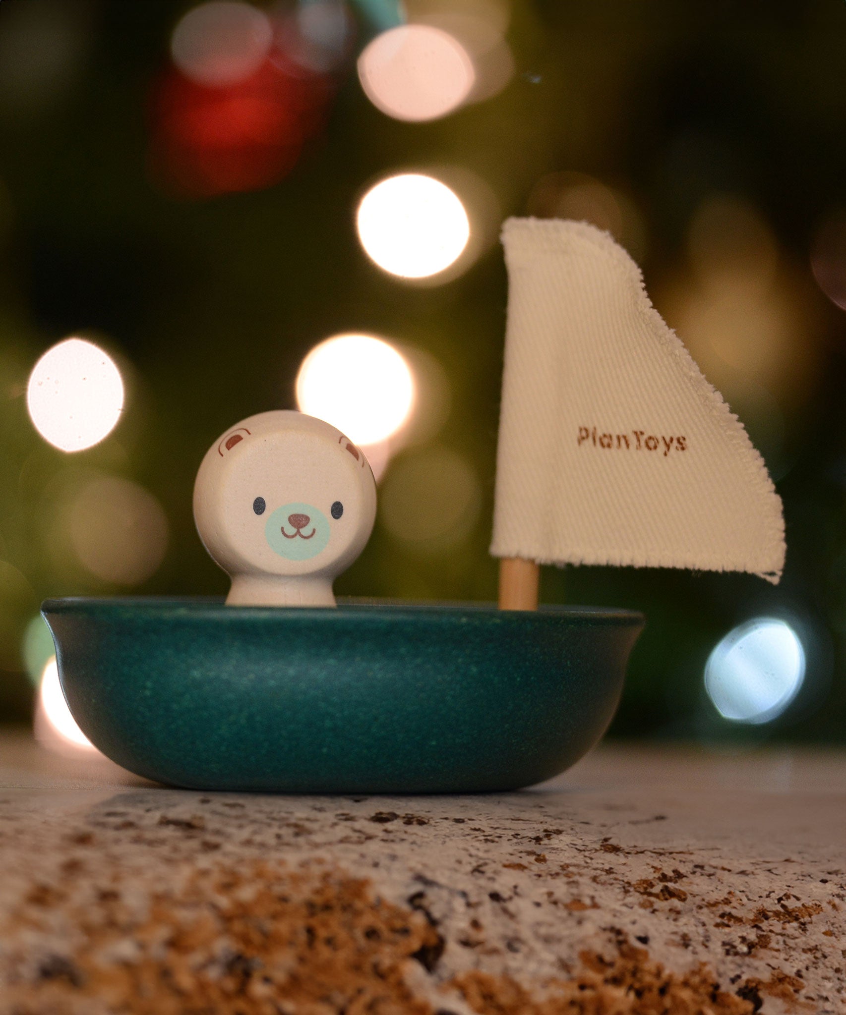 The Plan Toys Polar Bear Sailing Boat pictured with fairy lights behind. The blurred background is showing the bokeh from the lights. 