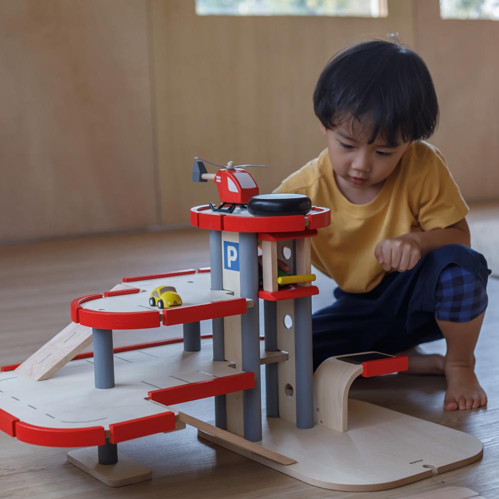 A child playing with the PlanToys Helicopter, the child has placed in on the helipad of the PlanToys parking garage. 
