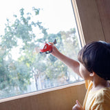 A child playing with the PlanToys Helicopter, the child is holding it up in front of a window, pretending to fly around. 