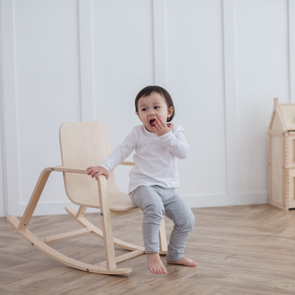 A child sitting on a PlanToys children's Rocking Chair. 