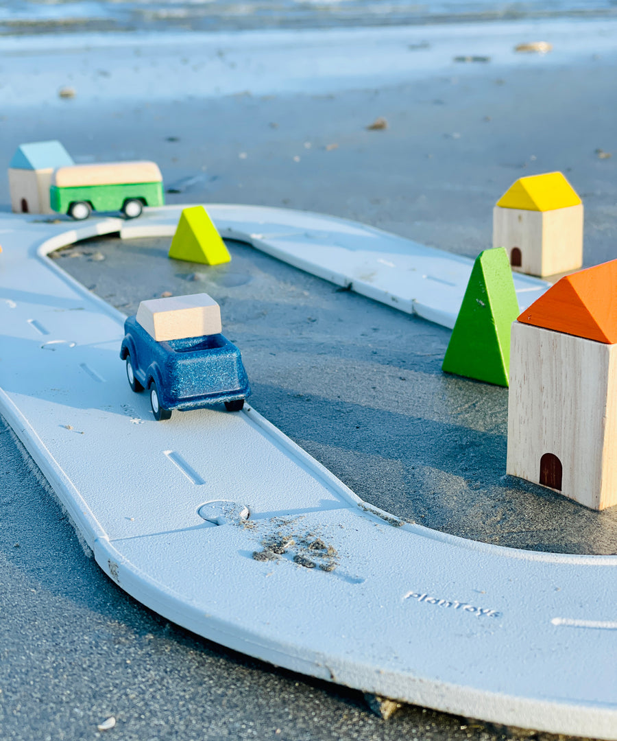 A Plan Toys Rubber Road and Rail Set placed on sand with PlanToys vehicles on.