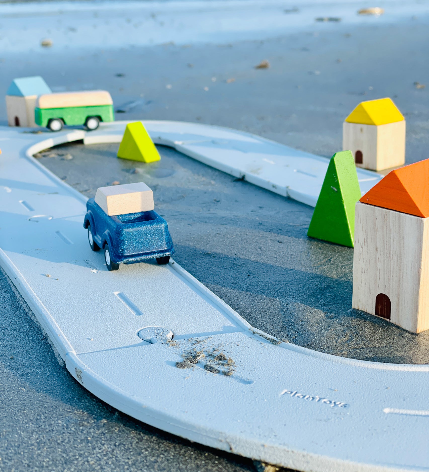 A Plan Toys Rubber Road and Rail Set placed on sand with PlanToys vehicles on.