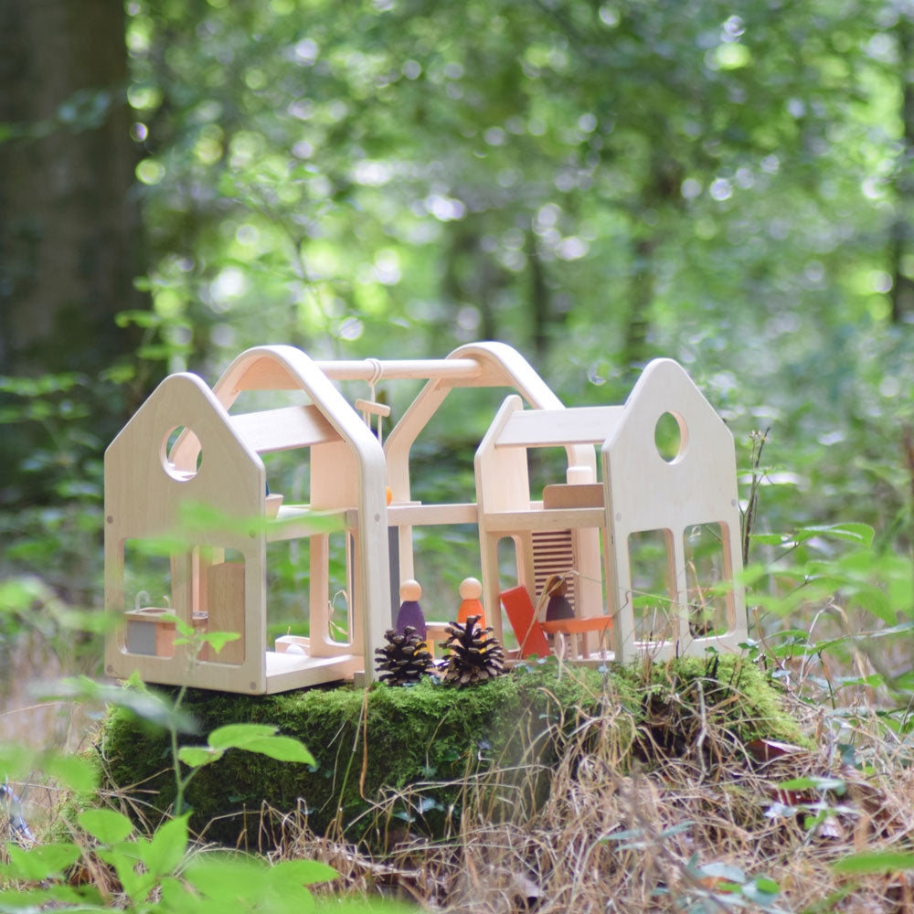 The PlanToys Slide N Go Dolls' House placed on a low moss covered tree stump in a forest. 