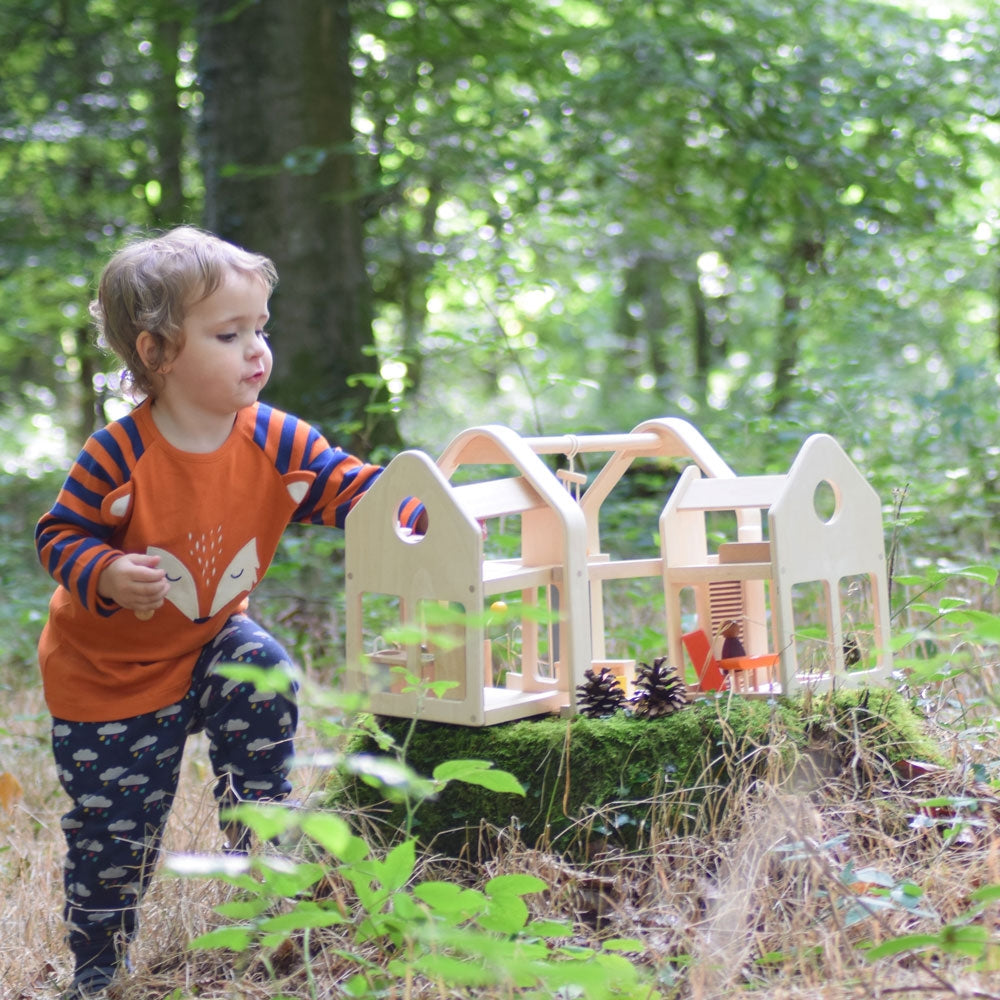 A child playing with the PlanToys Slide N Go Dolls' House placed on a moss covered tree stump in the forest. 