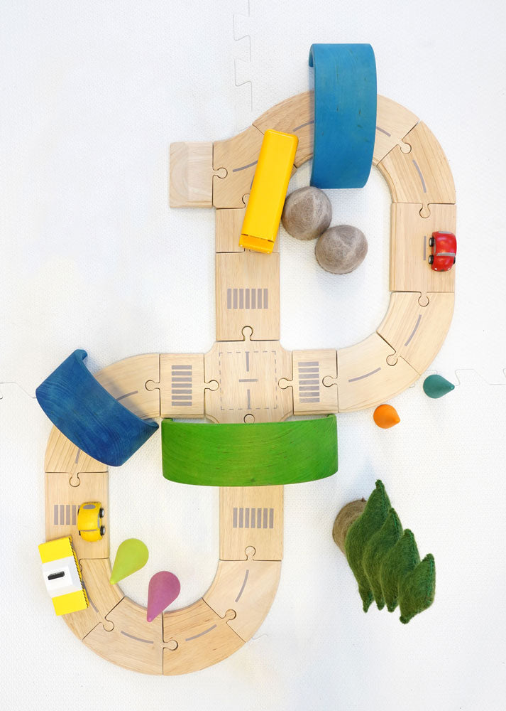 Plan Toys Standard Road System pictured from above with pieces of a Grimm's rainbow used as tunnels and bridges over the road