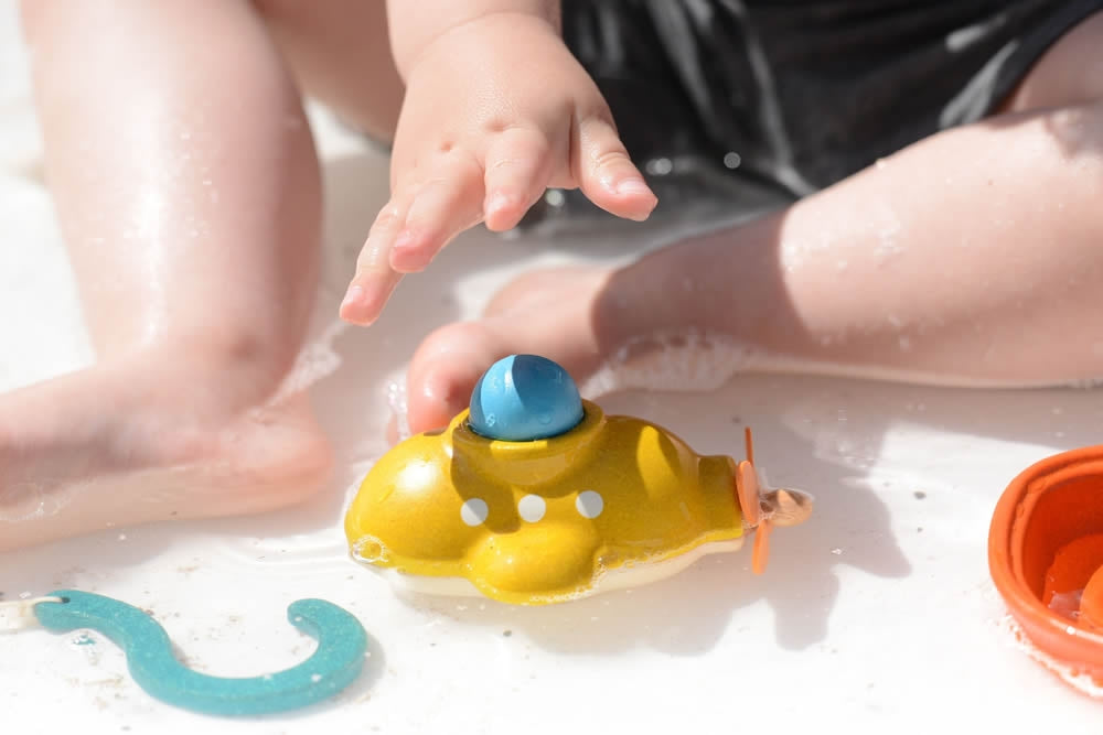 A child playing with the PlanToys submarine bath toy in shallow water. 