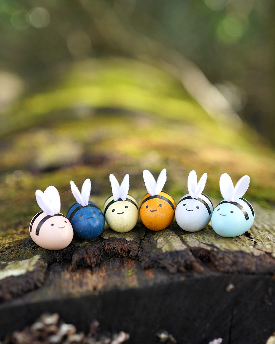 The bees from the PlanToys Bee Hives in the Orchard colour way placed in a line on a moss covered log. 