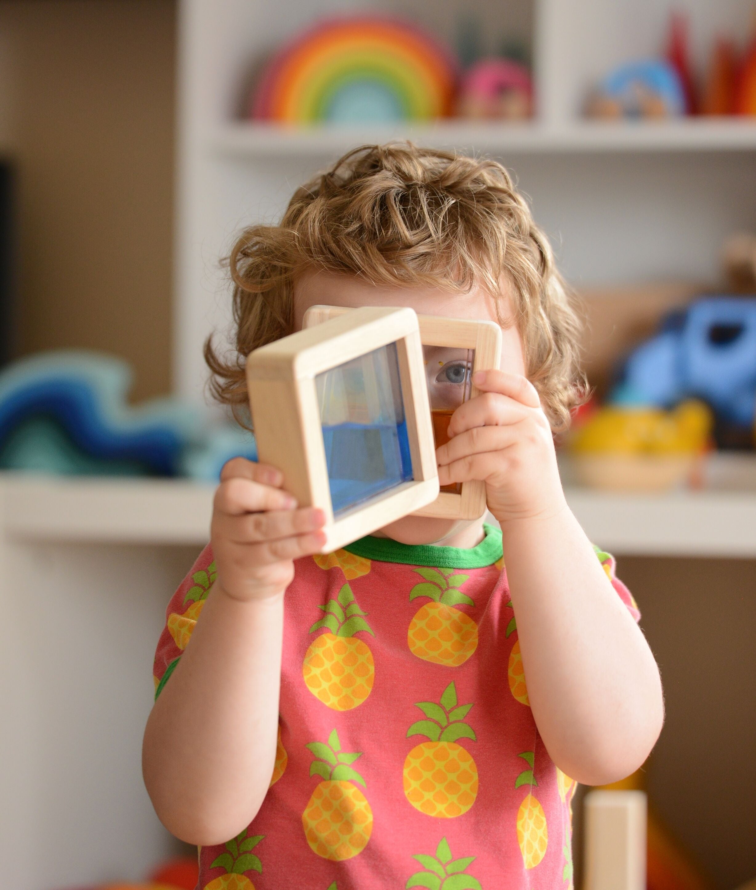 A child holding up two of the squared shaped Plan Toys Water Blocks peeping through them. 