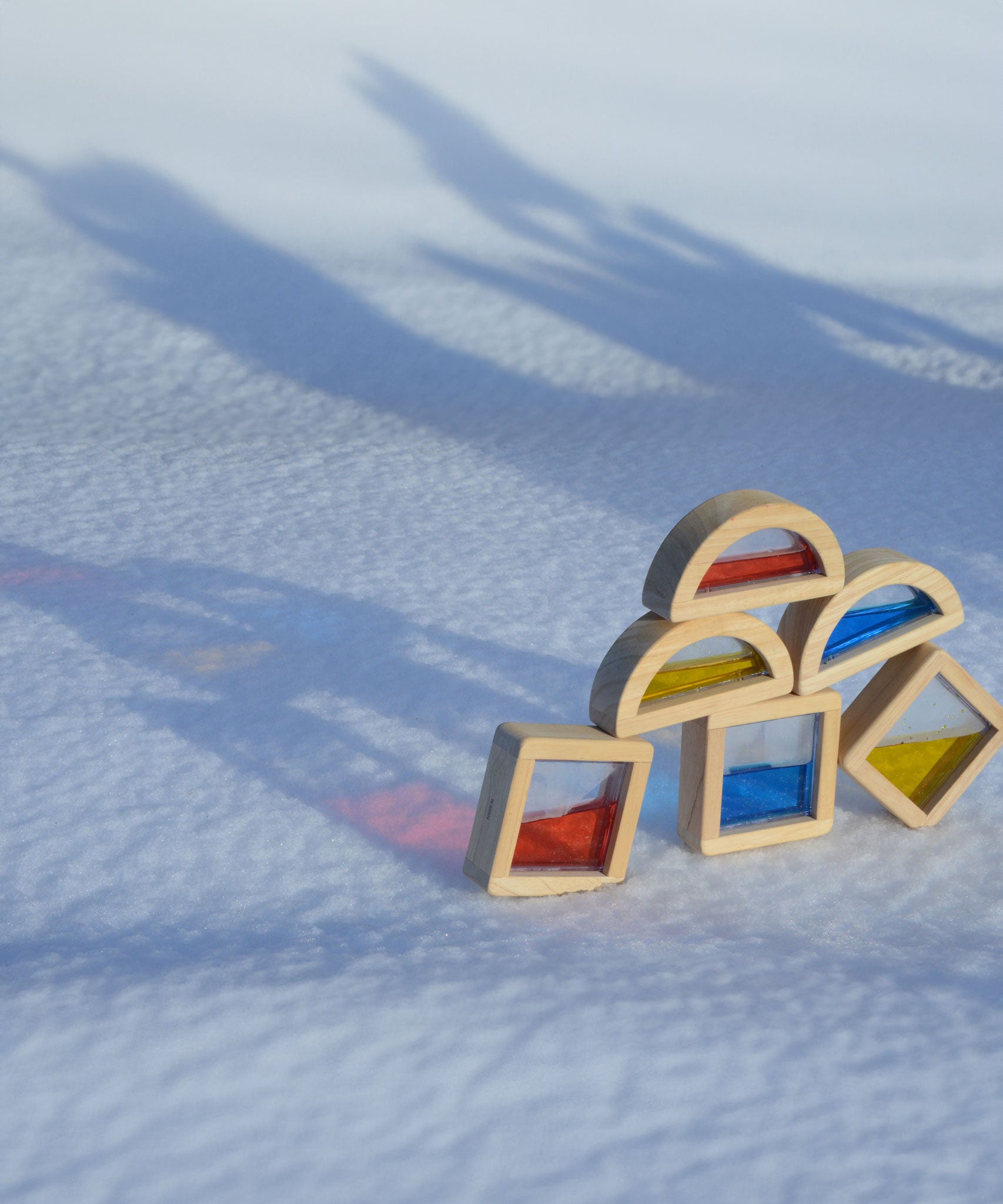 Plan Toys Water Blocks placed outdoors on snow. The reflection of colours from the blocks can be seen on the snow. 
